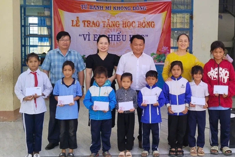 Thầy Vũ Văn Tùng (hàng sau, thứ 3 từ trái sang, người phụ trách "Tủ bánh mì 0 đồng") phối hợp với Ban Giám hiệu Trường Tiểu học và THCS Lê Văn Tám trao học bổng cho học sinh vượt khó học giỏi của trường. Ảnh: Văn Tùng