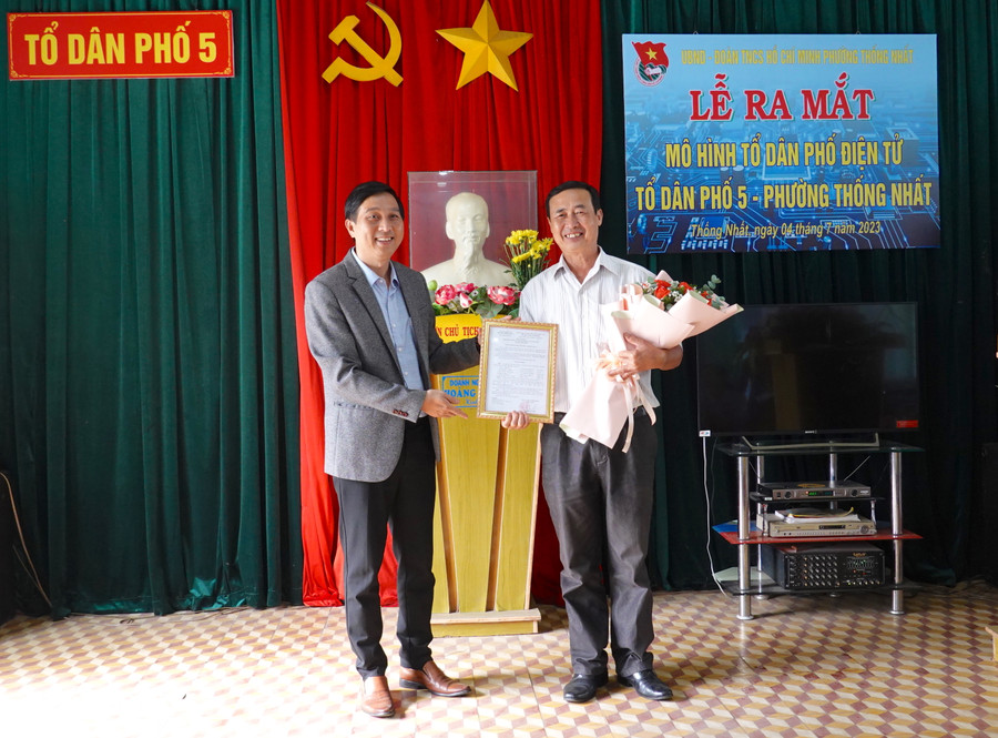 Chủ tịch UBND phường Thống Nhất Phạm Toàn Vinh (bìa trái) trao quyết định thành lập và tặng hoa chúc mừng cho Tổ tuyên truyền, hướng dẫn mô hình &quot;Tổ dân phố điện tử&quot; của Tổ dân phố 5. Ảnh: Mộc Trà
