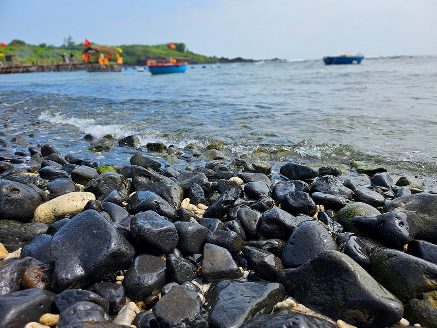 Dưới nắng xuân óng vàng, mặt nước biển càng trở nên trong xanh. Bãi đá đen trông giống hệt như những quả trứng đủ hình thù nằm san sát, uốn lượn vòng cung bao bọc quanh bờ vô cùng đẹp mắt. Ảnh: Mộc Trà