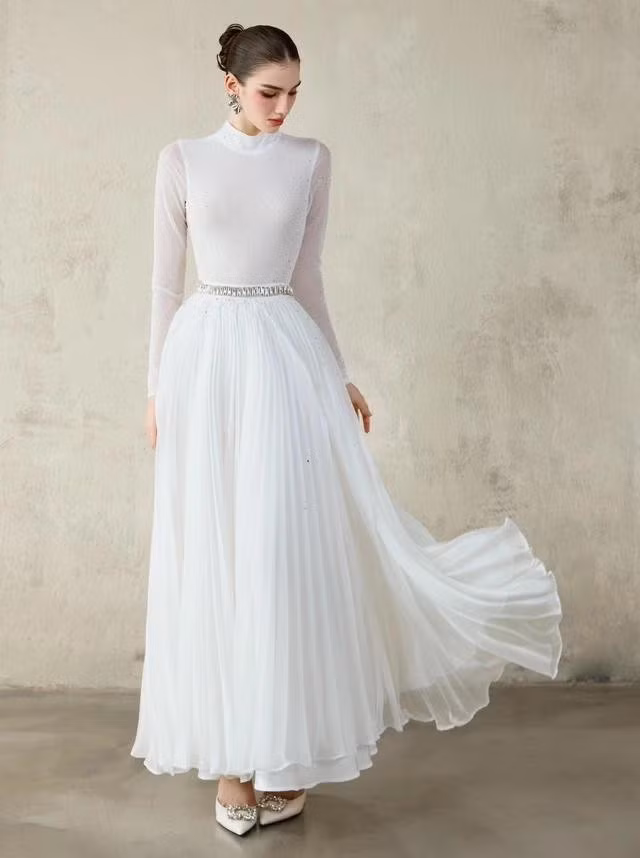 Đầm tiệc kín đáo dành cho những quý cô ưa chuộng phong cách trang nhã, quyến rũ cổ điển với phần thân trên là vải dệt kim mỏng nhẹ đính kết và tùng váy xếp ly hai lớp; gam màu trắng hoàn hảo cho mọi bữa tiệc và mọi vóc dáng