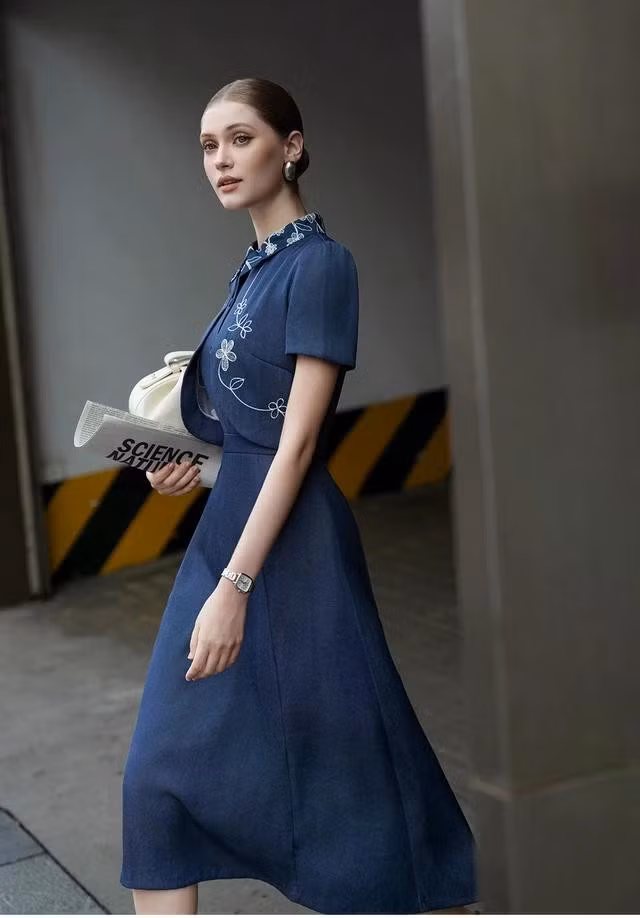 Thêm một ý tưởng cho nàng đi làm, đi học với thiết kế váy midi màu xanh denim có điểm nhấn thêu hoa trên cổ và vạt áo. ẢNH: NEM FASHION