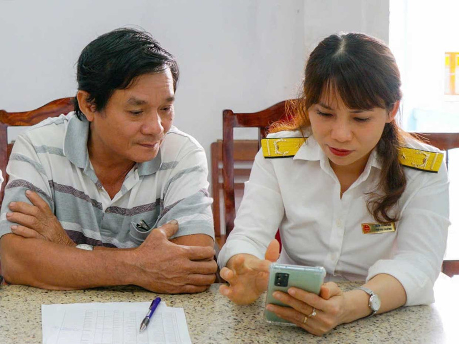 Công chức Thuế cơ sở 1 hỗ trợ NNT cài đặt nộp thuế điện tử trên thiết bị điện thoại di động. Ảnh: T.Sỹ