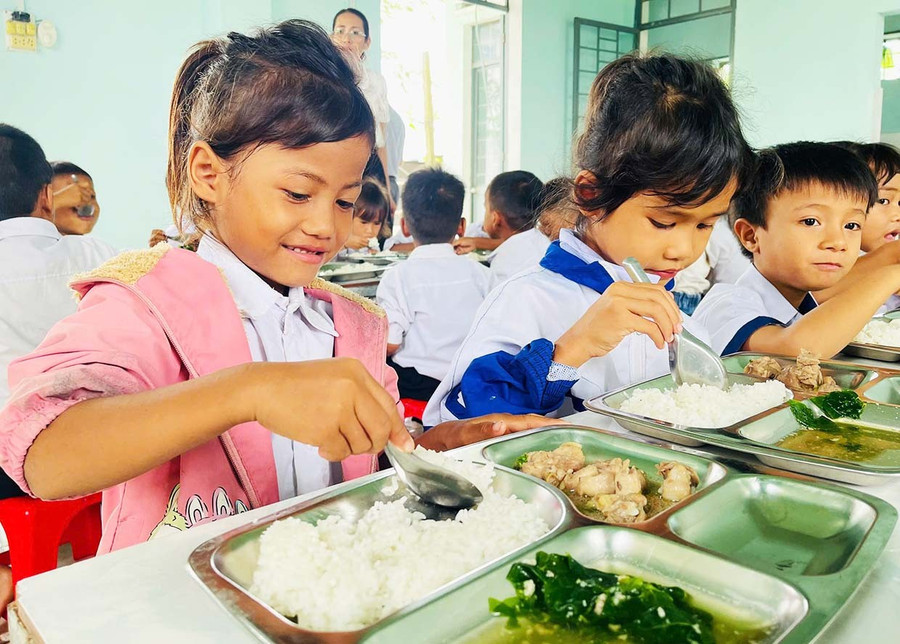 Em Siu H’Duyên (bìa trái, lớp 1.1, Trường Tiểu học và THCS Đinh Núp, xã Pờ Tó) vui mừng khi được ăn bữa cơm có thịt tại trường. Ảnh: Vũ Chi