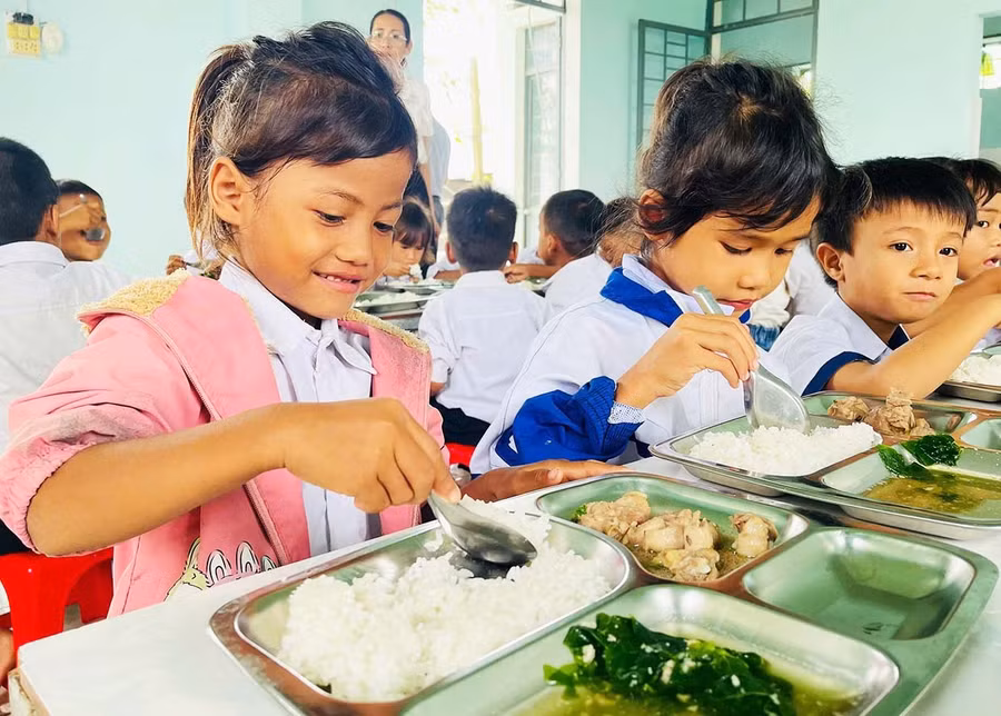 Em Siu H’Duyên (bìa trái, lớp 1.1, Trường Tiểu học và THCS Đinh Núp, xã Pờ Tó) vui mừng khi được ăn bữa cơm có thịt tại trường. Ảnh: Vũ Chi