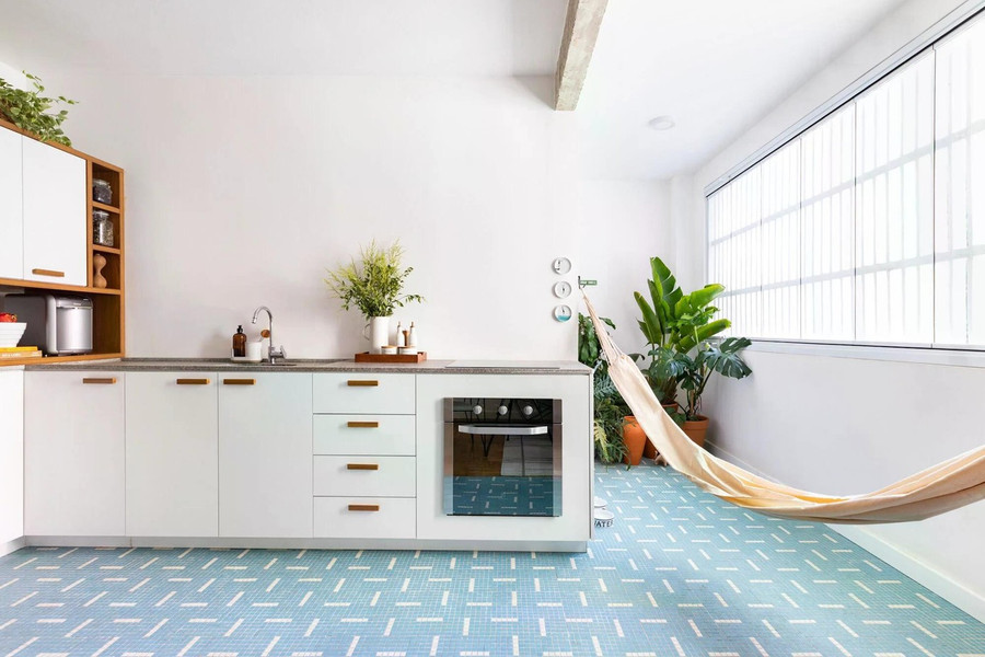 Khu bếp liền kề được thiết kế gọn gàng với tủ bếp trắng, mặt đá sáng và sàn gạch mosaic xanh nhạt