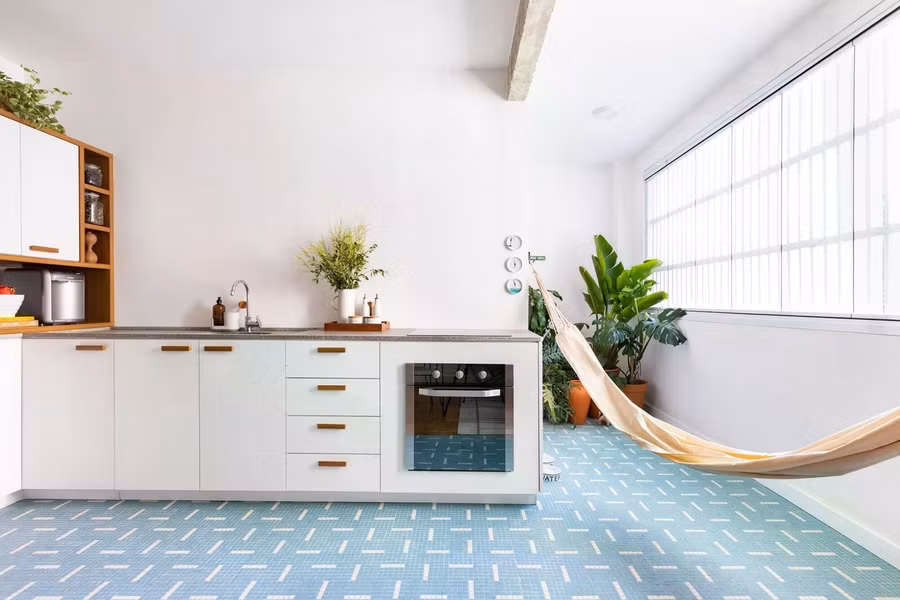 Khu bếp liền kề được thiết kế gọn gàng với tủ bếp trắng, mặt đá sáng và sàn gạch mosaic xanh nhạt