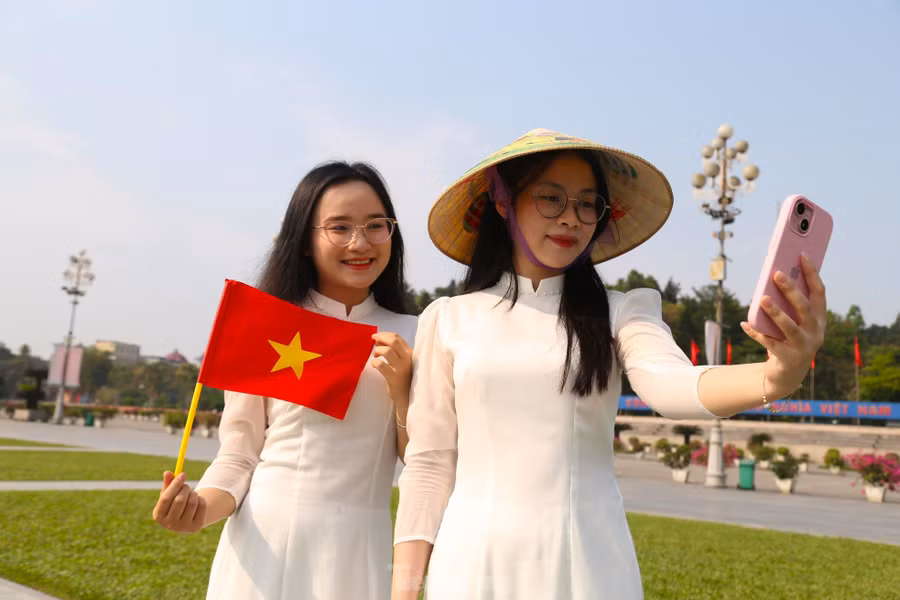 Đôi bạn “song Thương”, Hứa Thị Hoài Thương và Nguyễn Thị Thương (sinh viên trường Đại học Vinh) rạng rỡ trong trang phục áo dài trắng cùng lá cờ Tổ quốc và chiếc nón lá.