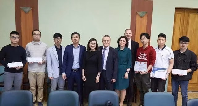 Cô Anisova Tatyana Leonidovna (váy xanh) chụp ảnh cùng các sinh viên Ngô Duy Khánh (ngoài cùng bên trái), Trần Văn Mạnh (thứ 2 từ phải sang), Phạm Quốc Việt (thứ 3 từ phải sang) tại buổi gặp gỡ của nhà trường với phái đoàn của Đại sứ quán Việt Nam. ẢNH: NVCC