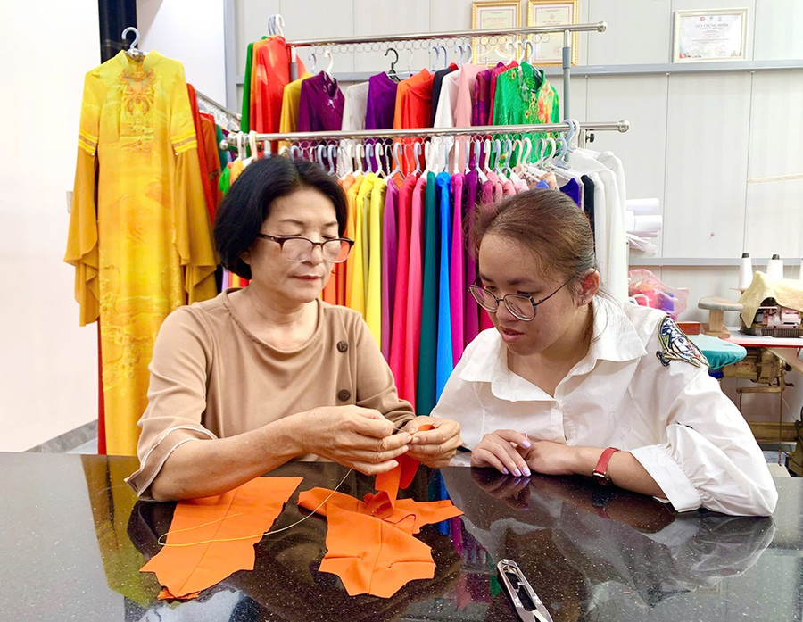 Nhà thiết kế Nguyễn Hạnh (bìa trái) hướng dẫn chị Trương Thị Thanh Huyền kỹ thuật may áo dài mini size. Ảnh: C.H 0bg.jpg