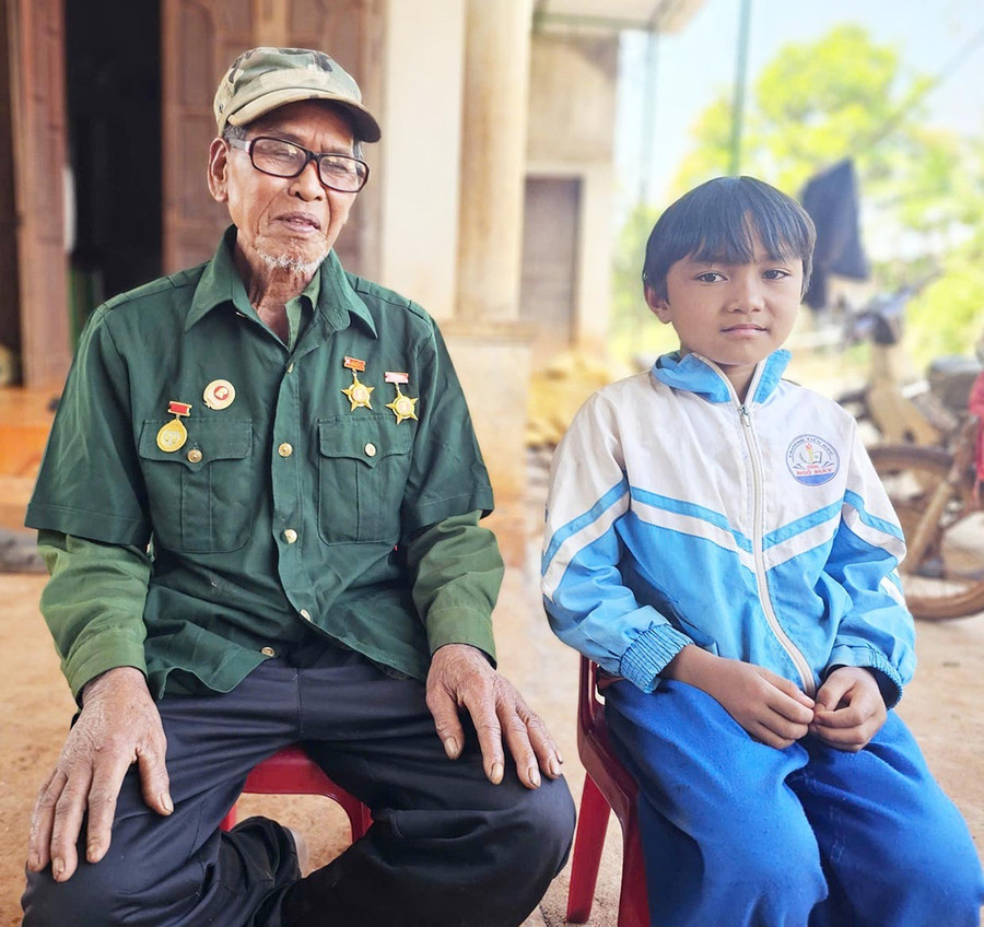 Ông Rơ Châm Hăng kể lại cho cháu trai của mình về những năm tháng chiến đấu. Ảnh: R’Ô HOK