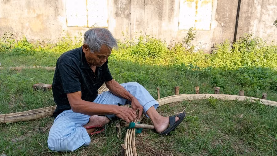 Ông Nguyễn Quang Thơ đang ngồi nứt vành (cố định vành) của chiếc thuyền thúng. Ảnh: Mỹ Ly