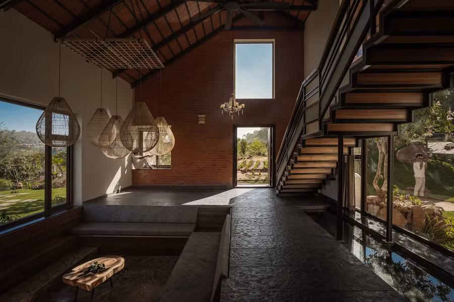 Phòng khách được bố trí thấp hơn nhẹ so với mặt bằng chính, nằm giữa hồ bơi bên ngoài và hồ cá koi tĩnh lặng bên trong - một dụng ý thiết kế khéo léo nhằm tăng cường cảm nhận về không gian. Một cầu thang đơn nhịp kéo dài dọc theo không gian sinh hoạt tạo điểm nhấn về chiều cao và chiều sâu, đồng thời làm nổi bật thể tích trần cao gấp đôi.