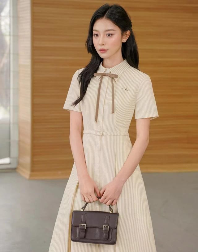 Váy sơ mi dáng dài ghi điểm với tông màu vàng pastel dịu mát, họa tiết sọc dọc tôn dáng giúp nàng thon gọn và ưa nhìn hơn. Thiết kế điểm chi tiết nơ, đai eo và họa tiết thêu xinh xắn tăng thêm điểm cộng về thẩm mỹ. ẢNH: JM