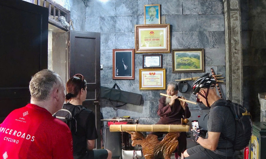 Du khách quốc tế đến thăm đền Thái Vi thích thú ghi lại hình ảnh cụ Thim biểu diễn âm nhạc dân tộc, sử dụng nhiều loại nhạc cụ truyền thống. Ảnh: Đình Minh