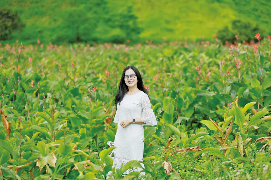 Ms. Bui Ngoc Nga takes a photo with canna flowers at the foot of Chu Dang Ya mountain. Photo: NVCC Bà Bùi Ngọc Ngà chụp ảnh với hoa dong riềng dưới chân núi Chư Đang Ya.