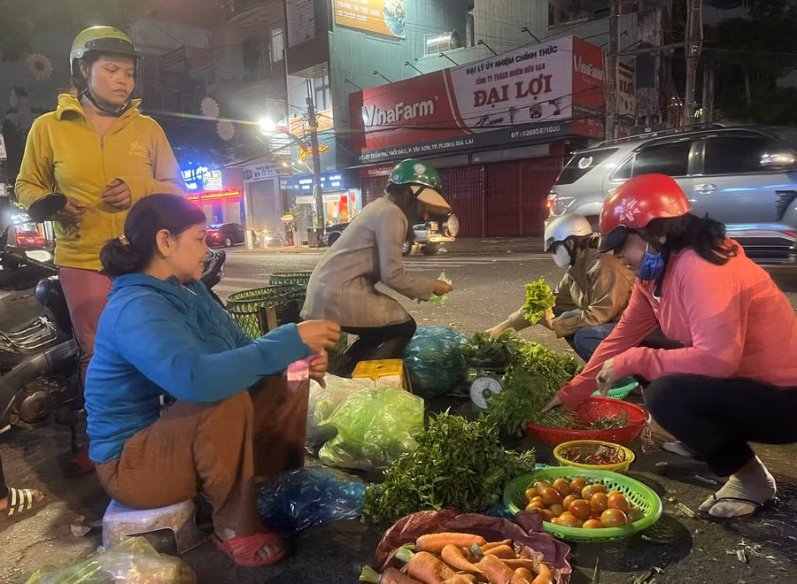 Chị Lai (áo xanh) ngồi nán lại muộn hơn để cố bán cho hết số rau, củ. Ảnh: P.D