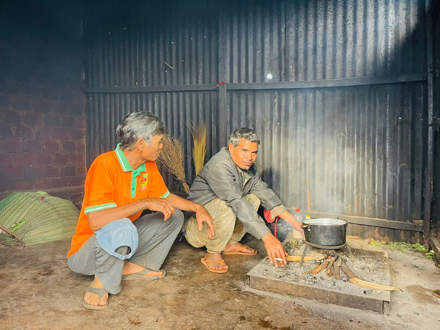 Ông A Minh (áo cam, ngồi bên cạnh anh Nik) thường xuyên sang thăm hỏi, hỗ trợ nhu yếu phẩm cho gia đình bà Plăi. Ảnh: Nhật Hào Ông A Minh (áo cam, ngồi bên cạnh anh Nik) thường xuyên sang thăm hỏi, hỗ trợ nhu yếu phẩm cho gia đình bà Plăi. Ảnh: Nhật Hào