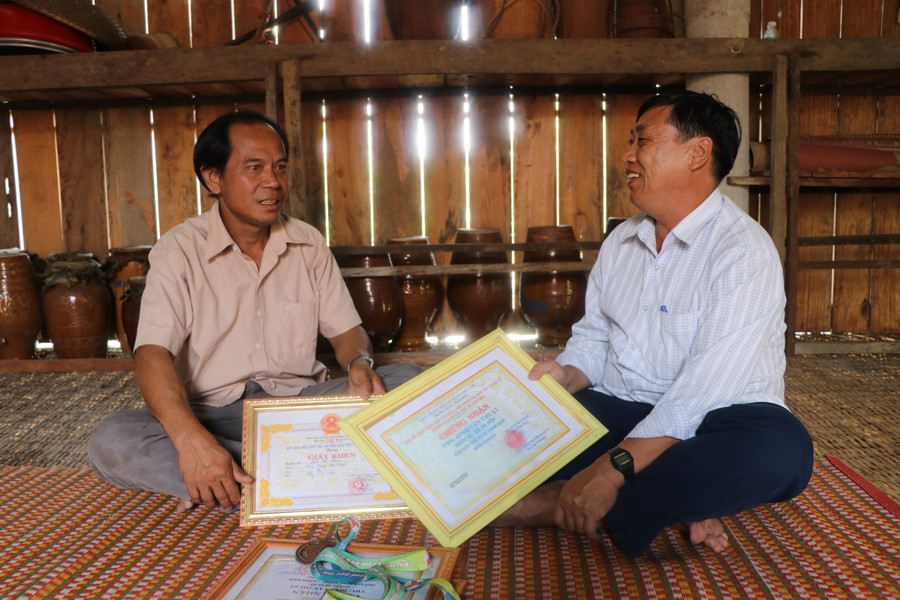 Ông Đinh Văn Nhin (bìa trái) tự hào kể về những thành tích gia đình đạt được trong môn thi chạy cà kheo với ông Lý Văn Thắng-công chức Văn hóa-Xã hội xã Ya Hội, huyện Đak Pơ. Ảnh: Ngọc Minh