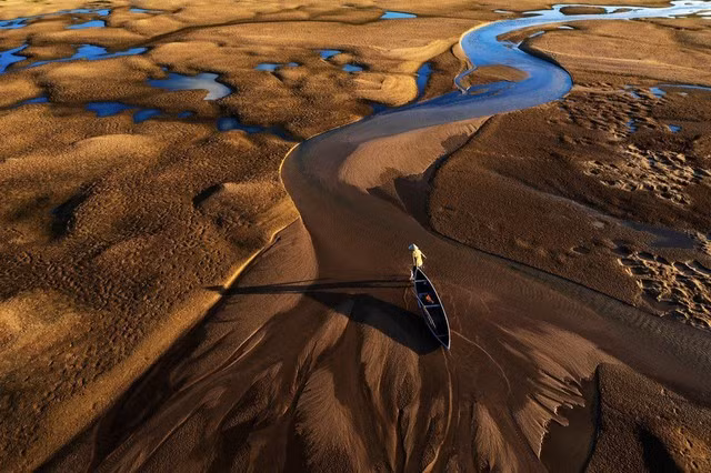 Trở về của tác giả Lê Chí Trung được đánh giá cao ở hạng mục Con người. Anh cho biết ảnh chụp ở hạ lưu sông Kỳ Lộ, Phú Yên, vào những ngày thủy triều xuống thấp, sau khi bắt cá xong người dân men theo những dòng nước cạn để trở về nhà trong ánh nắng chiều tạo nên bức tranh cuộc sống bình dị. "Trong một lần dừng chân ở cầu gỗ, tôi dùng flycam để quan sát tổng thể khung cảnh thì ngỡ ngàng phát hiện những bãi cát ven sông, đặc biệt là dòng nước uốn lượn với nhiều hình dáng lạ mắt", anh Lê Chí Trung chia sẻ.