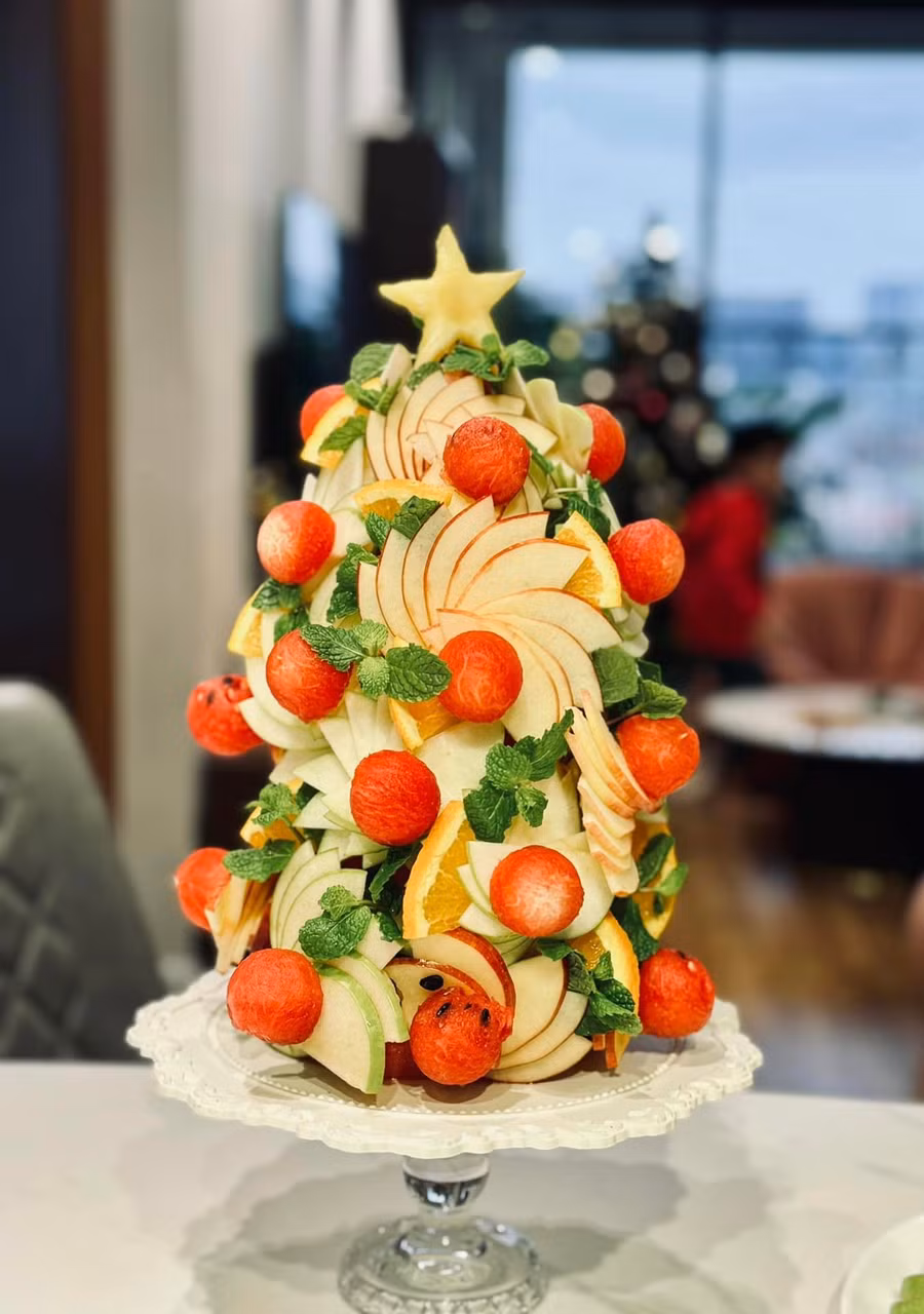 Sau khi gắn quả châu làm bằng dưa hấu lên bông hoa táo, chị gắn các bông hoa đó vòng quanh thân miếng dưa hấu theo đường chéo từ trên xuống. Ảnh: NVCC