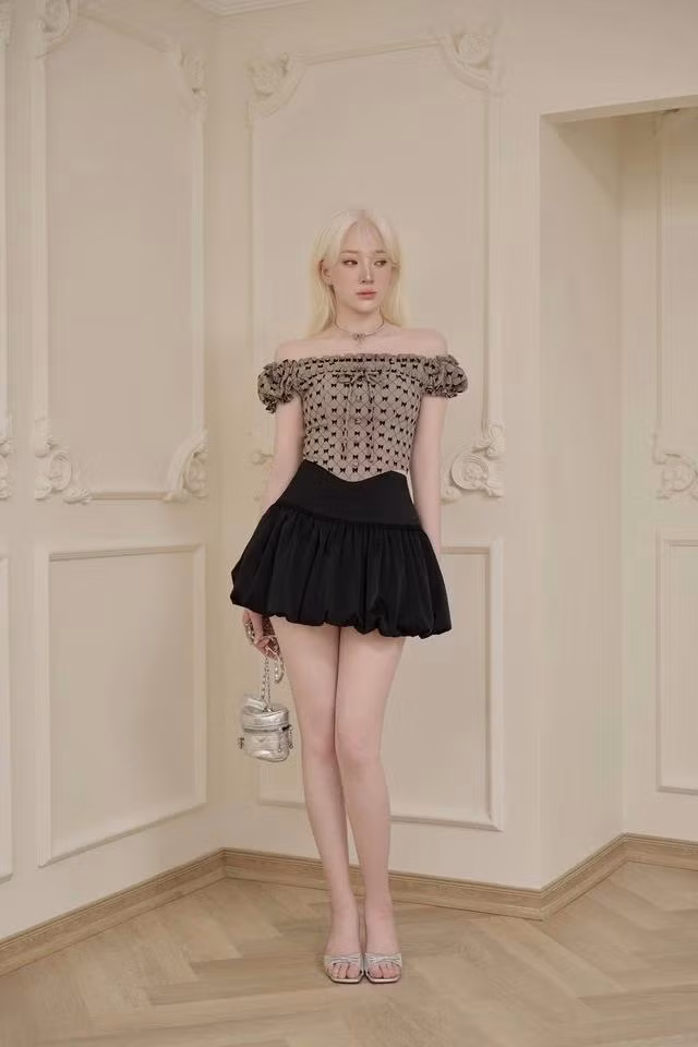 Trở thành một nàng thơ xinh đẹp, năng động nhưng không kém phần sang chảnh, quyến rũ với áo trễ vai phối chân váy bí ngô. Họa tiết monogram nơ nữ tính kết hợp phần gọng ôm phom tôn lên vòng 1 và eo thon của nàng. Chân váy có độ phồng, cạp cao phối viền ren đen nhấn nhá tạo nên vẻ điệu đà đặc trưng của các cô gái