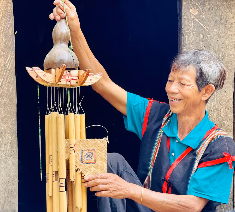 Ông Byơh bên chiếc chuông gió cổ hình cây nêu do chính tay ông chế tác. Ảnh: Trần Dung