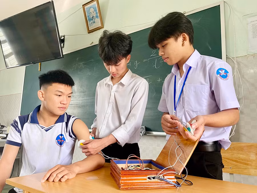 Từ phải sang: Em Nguyễn Cường và Lê Trần Tuấn Anh theo dõi tình trạng sức khỏe của bạn Bùi Việt Hưng (lớp 12D2, Trường THPT Pleiku) bằng thiết bị giám sát sức khỏe. Ảnh: Mộc Trà