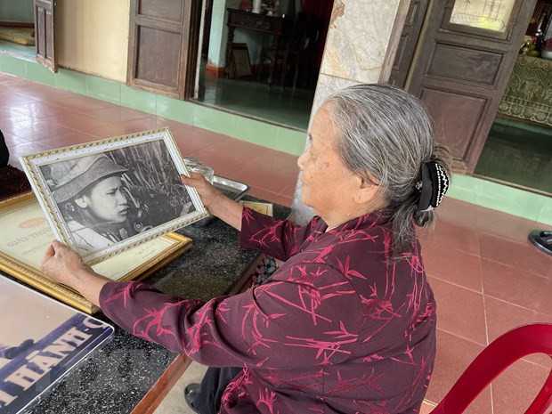 Bà Hoàng Thị Chẩm với bên bức hình được chụp khi còn là du kích bắn tỉa tại Căn cứ quân sự Dốc Miếu. (Ảnh: Thanh Thủy/TTXVN)