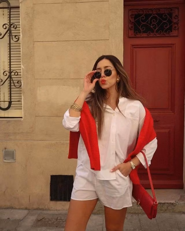 Cách tạo kiểu được ưa chuộng trong mùa thu đông - vắt áo len lên vai vẫn có thể áp dụng cho mùa hè thu dù bộ đôi quần shorts vải linen và sơ mi cotton thoáng mát được kết hợp. Áo và túi xách, giày và màu son tạo nên điểm nhấn tone sur tone cho bản phối này. ẢNH Cecilia