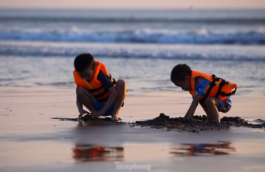 Những em nhỏ vui đùa xây lâu đài cát trên bãi biển.