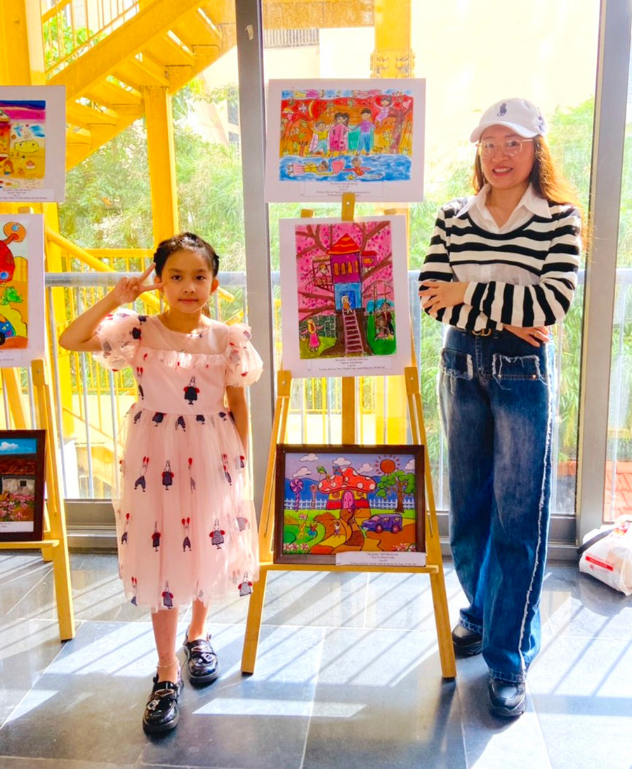 Bé Nguyễn Lê An Chi cùng mẹ chụp ảnh lưu niệm bên bức tranh đạt giải triển vọng của mình (tranh trên cùng) tại buổi trao giải cuộc thi vẽ tranh "Ngôi nhà mơ ước". Ảnh NVCC Bé Nguyễn Lê An Chi cùng mẹ chụp ảnh lưu niệm bên bức tranh đạt giải triển vọng của mình (tranh trên cùng) tại buổi trao giải cuộc thi vẽ tranh "Ngôi nhà mơ ước". Ảnh NVCC