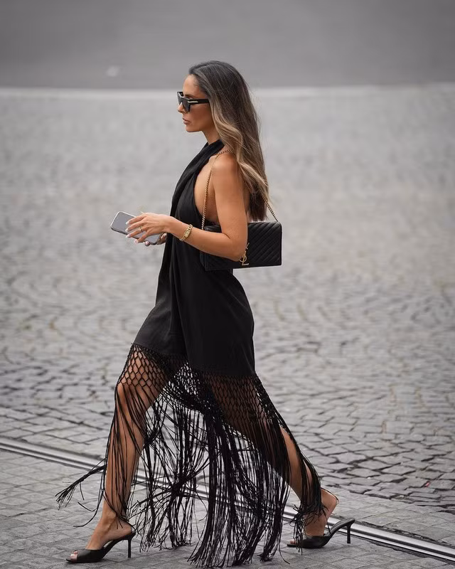 Tua rua chính là phong cách nổi bật nhất trên sàn diễn xuân hè năm nay. Rất nhiều tín đồ đã lựa chọn chi tiết này để xuống phố dạo chơi. Nếu chưa biết cách diện chúng thế nào để chuẩn thời thượng, bạn hãy tham khảo ngay set đồ của Pipa Tavares. Cô nàng lựa chọn một chiếc váy đen tối giản cùng điểm nhấn là phần tà váy tua rua và kết hợp cùng sandal mules