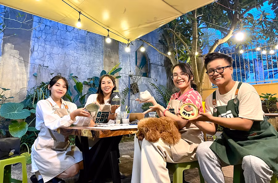Bạn trẻ Nguyễn Ngọc Như Quỳnh-chủ tiệm gốm Bàn Xoay (bìa phải) và khách trải nghiệm bên những sản phẩm vừa hoàn thiện. Ảnh: Lam Nguyên