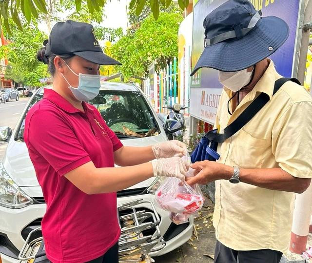 Chị Đặng Thuỵ Nhật Hân (bên trái), chủ tiệm giúp khách trao tận tay bánh mì cho người khó khăn. Ảnh: NVCC
