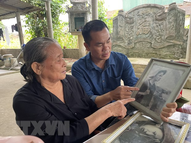 Bà Hoàng Thị Chẩm với bên bức hình được chụp khi còn là du kích bắn tỉa tại Căn cứ quân sự Dốc Miếu. (Ảnh: Thanh Thủy/TTXVN)