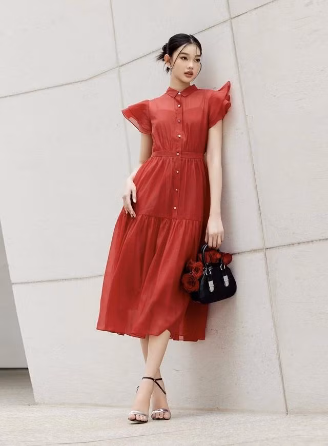 Màu đỏ là màu sắc đại diện cho sự kiêu hãnh và lòng nhiệt huyết. Trong thời trang, sắc đỏ luôn giúp người mặc tỏa sáng và quyến rũ, lan tỏa thông điệp tinh tế về cảm xúc mãnh liệt. Váy sơ mi màu đỏ trên chất vải tơ organza chính là sự cộng hưởng của phong thái sang trọng, kiêu kỳ đầy quyền lực