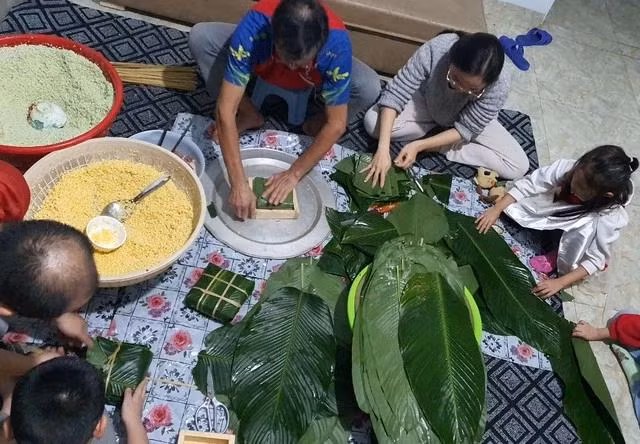 Gia đình quây quần gói bánh chưng, gạo được trộn với nước lá riềng tươi để khi bánh chín, phần gạo nếp luôn xanh mướt. ẢNH: BẢO VY