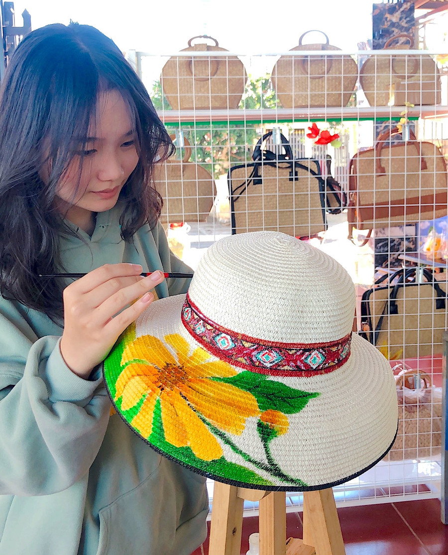 Em Lê Dương Bảo Vy vẽ trang trí hoa dã quỳ và họa tiết thổ cẩm trên chiếc mũ cói thô. Ảnh: Mộc Trà Em Lê Dương Bảo Vy vẽ trang trí hoa dã quỳ và họa tiết thổ cẩm trên chiếc mũ cói thô. Ảnh: Mộc Trà