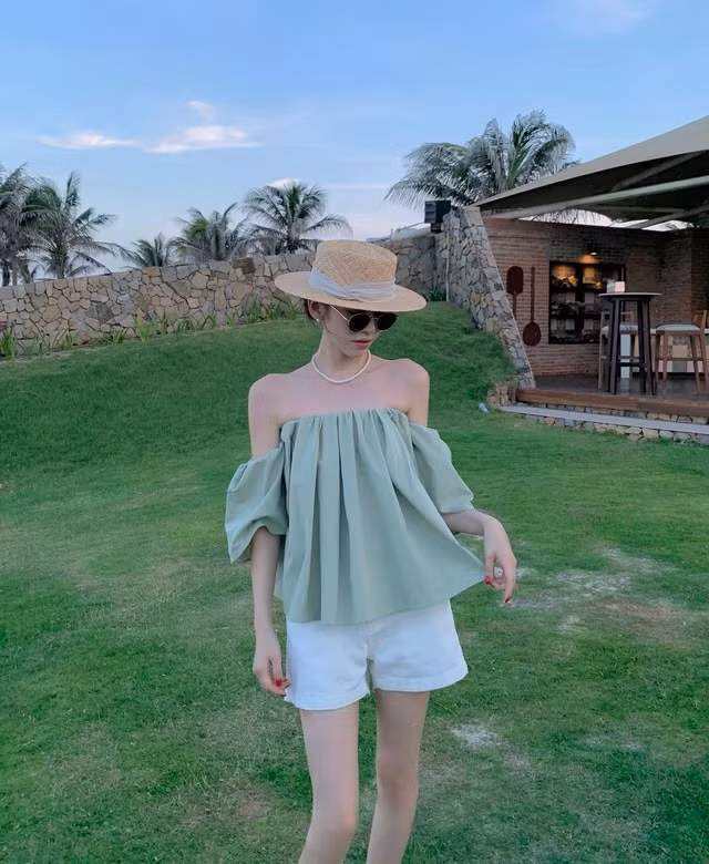 Thích nét nhẹ nhàng nữ tính, chị em hãy kết hợp quần shorts trắng với áo trễ vai màu xanh mint. Công thức này cho hiệu quả hack tuổi tốt. Để đảm bảo sự hài hòa cho tổng thể trang phục, chị em nên nhấn nhá bằng mũ cói, vòng cổ ngọc trai và kính râm đen.