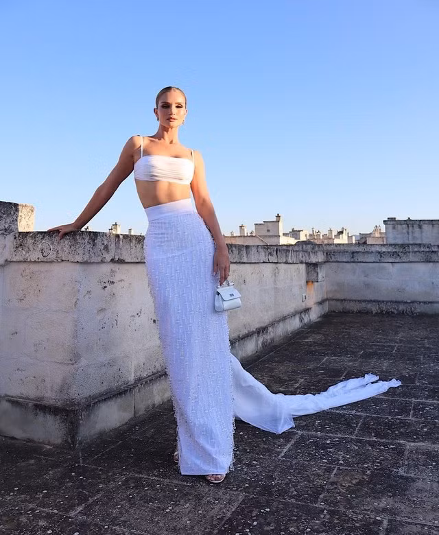 Rosie Huntington Whiteley khoe phong cách dự tiệc với cả cây all white đầy quyến rũ, sang trọng gồm chân váy maxi đuôi cá mix cùng áo bra rop hai dây. Kiểu tóc búi cao cùng với việc sử dụng khuyên tai ngắn, túi xách mini khiến cô ghi điểm tuyệt đối trong bữa tiệc.