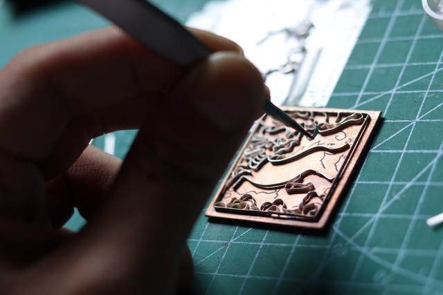 Tùng uốn cong những sợi kim loại theo hình họa tiết để tạo khuôn đổ men vào, sau đó đem nung với nhiệt độ phù hợp. Ảnh KIM NGỌC NGHIÊN Tùng uốn cong những sợi kim loại theo hình họa tiết để tạo khuôn đổ men vào, sau đó đem nung với nhiệt độ phù hợp. Ảnh KIM NGỌC NGHIÊN