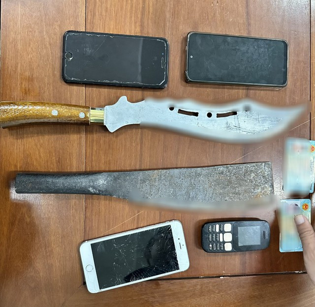 Đà Nẵng: Kinh hãi với đao, mã tấu thu được từ nhóm côn đồ chém người - Ảnh 1. 2 cây đao, mã tấu cùng điện thoại của nhóm côn đồ bị tạm giữ. Ảnh: NGUYỄN TÚ