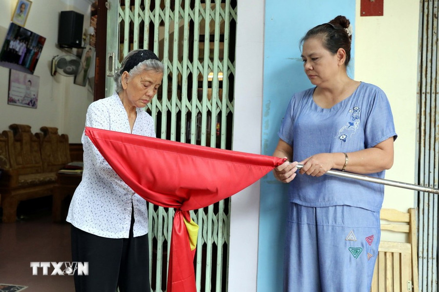 Bà Bạch Thị Khôi, cán bộ tiền khởi nghĩa ở phường Vĩnh Trại, thành phố Lạng Sơn, tỉnh Lạng Sơn cùng con gái treo cờ rủ để tưởng nhớ, tri ân Tổng Bí thư Nguyễn Phú Trọng. (Ảnh: Văn Đạt/TTXVN)