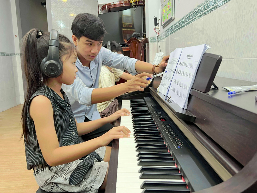 Hồ Lê Tri Thức dạy piano cho trẻ để vừa có thêm thu nhập, vừa trau dồi kinh nghiệm. Ảnh: D.L dam-me-am-nhac-1-7065.jpg