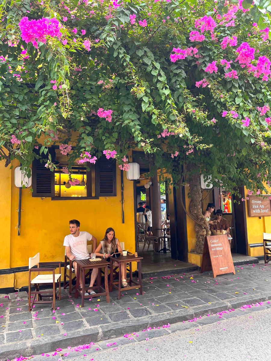 Du khách thưởng thức cà phê bên mái hiên, dưới giàn hoa giấy rực rỡ tại phố cổ Hội An. Ảnh: P.V img-7884.jpg