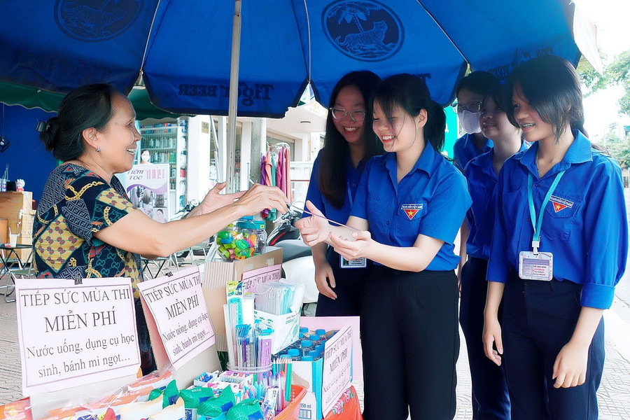 Bà Trần Thị Lý (bìa trái) hỗ trợ nước uống, bút... cho thí sinh, tình nguyện viên tại điểm thi Trường THPT Phan Bội Châu. Ảnh: Đ.T
