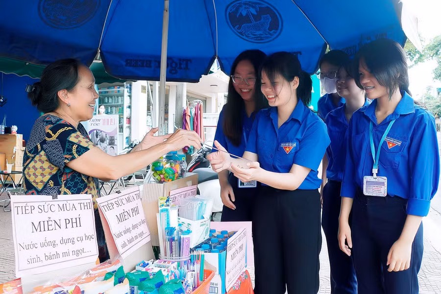Bà Trần Thị Lý (bìa trái) hỗ trợ nước uống, bút... cho thí sinh, tình nguyện viên tại điểm thi Trường THPT Phan Bội Châu. Ảnh: Đ.T