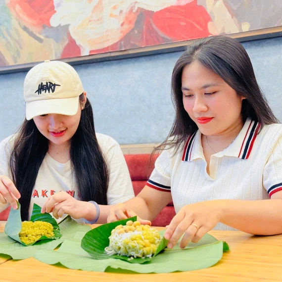 Chị Lê Thị Ni Na (bìa phải) gói xôi cốm cho khách hàng. Ảnh: M.K