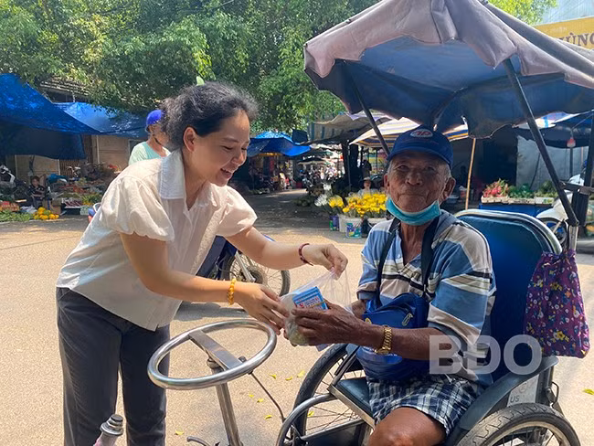 Phật tử trao cơm chay của chùa Phước Hưng cho một cụ già bán vé số tật nguyền. Ảnh: N.C