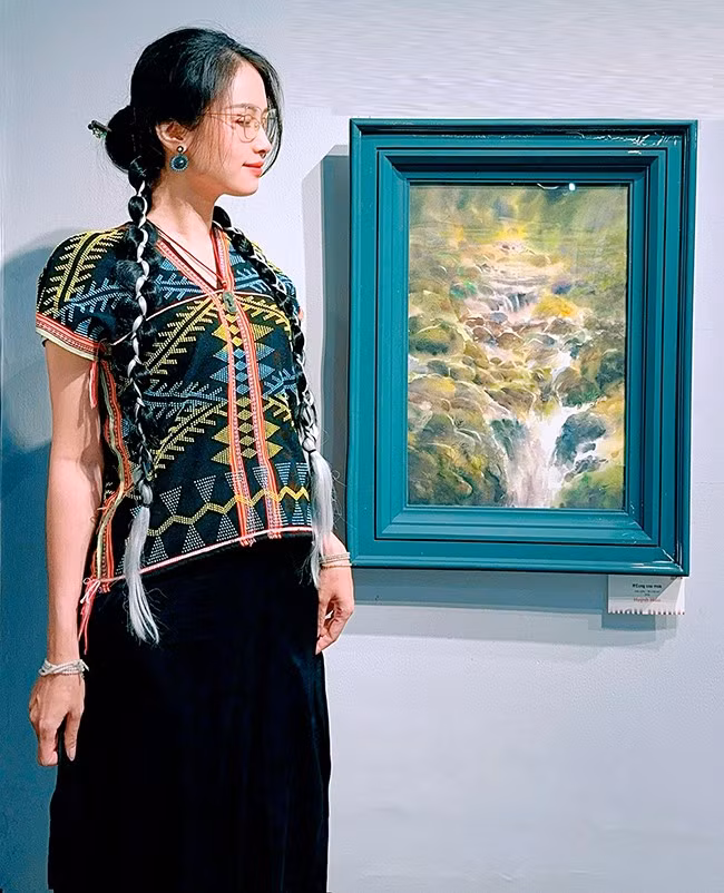 Họa sĩ Huỳnh Hiền bên tác phẩm Con suối nhỏ tham gia tại Triển lãm tranh và ký họa Màu nước 2025. Ảnh: NVCC